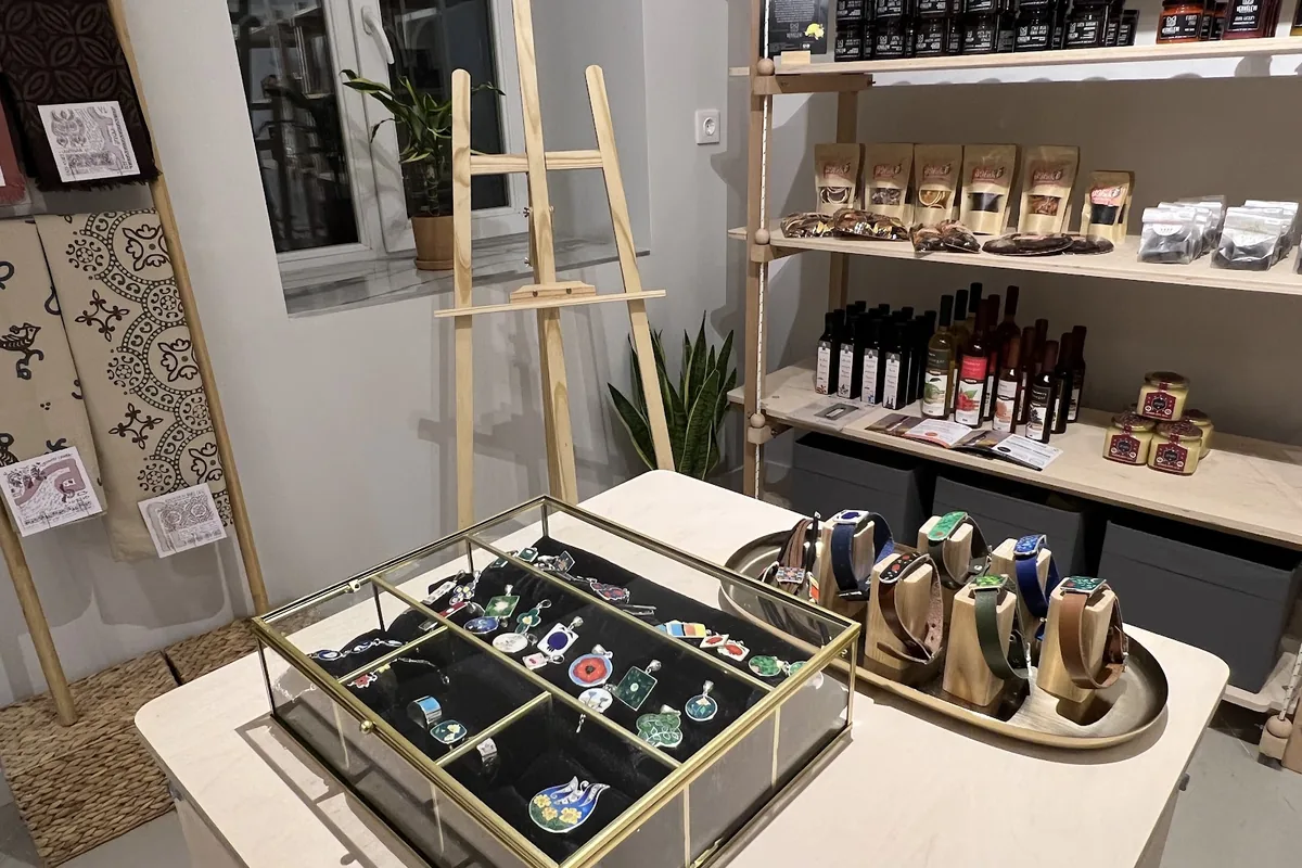 Enamel pendants in a glass case beside shelves of honey, sauces and bottled drinks inside OVOP in Vera
