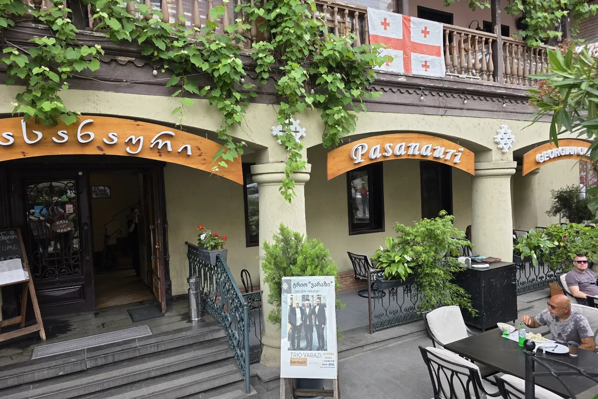 The arched facade of Pasanauri on Baratashvili Street, with its carved wooden sign, vine-hung balcony and terrace tables