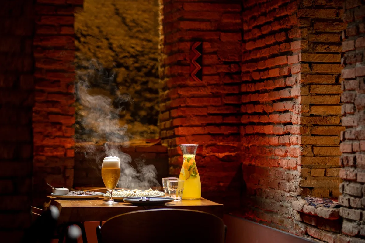 Brick-walled dining nook with a steaming plate and a glass of beer at Pictograma in Tbilisi