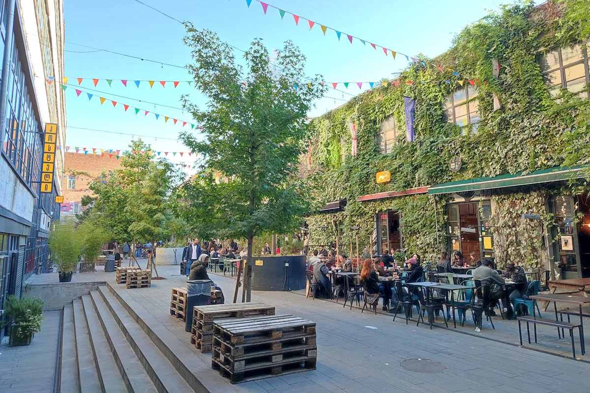 Courtyard tables under string bunting beside the ivy-covered factory wall outside PIPES Burger Joint