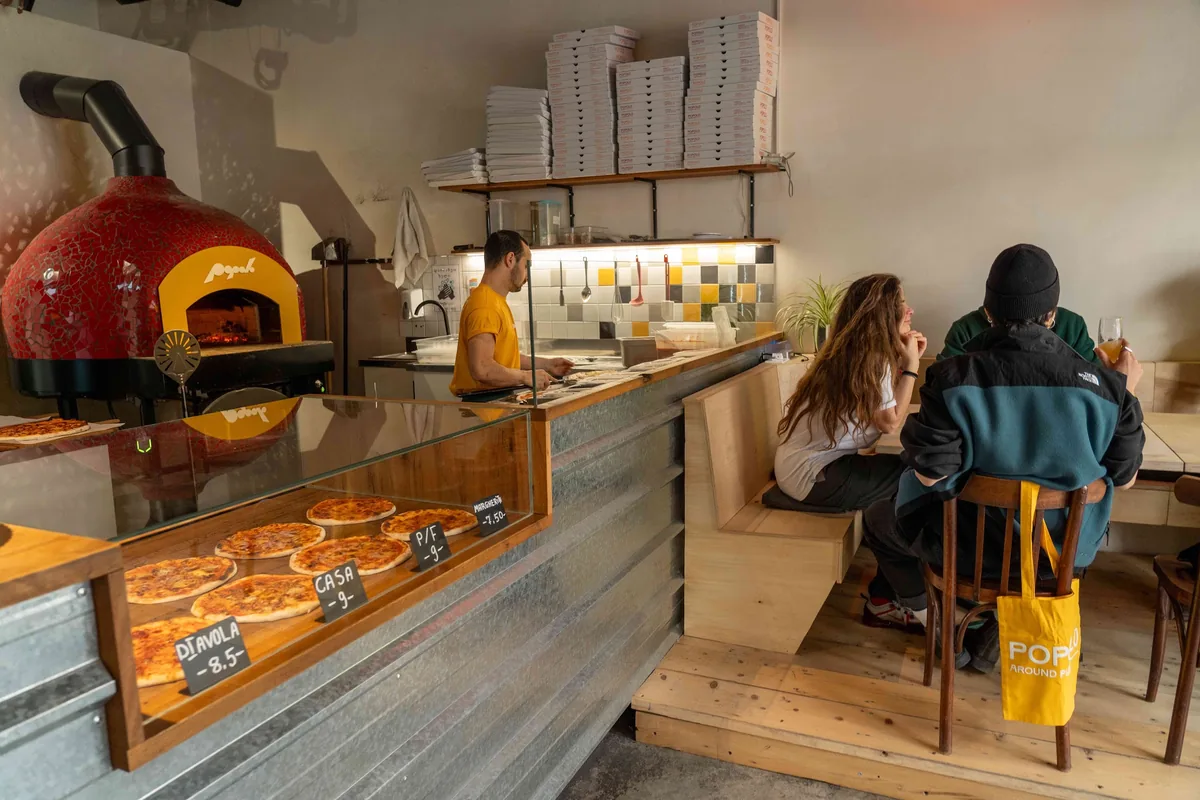 Pizzeria counter with a red wood-fired oven and diners at Popolo in Fabrika