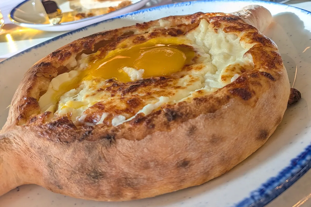 Adjarian khachapuri with an egg yolk on a blue-rimmed plate at Puri Guliani