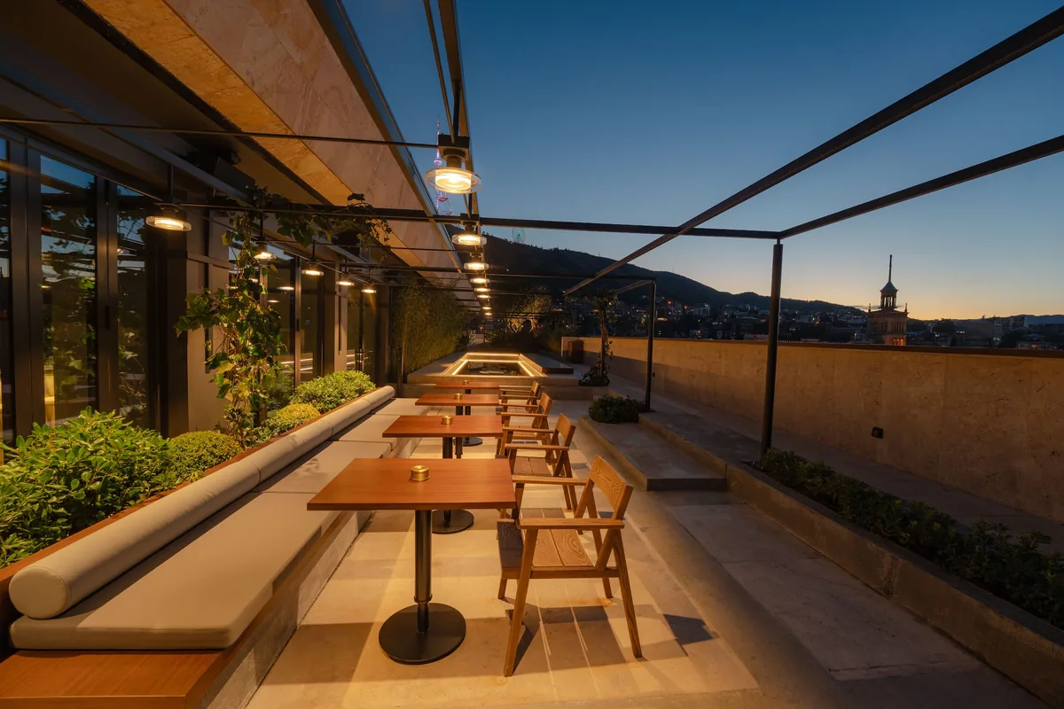 Rooftop terrace with wooden tables and banquette seating at twilight at Rolling Stone Rooftop Bar