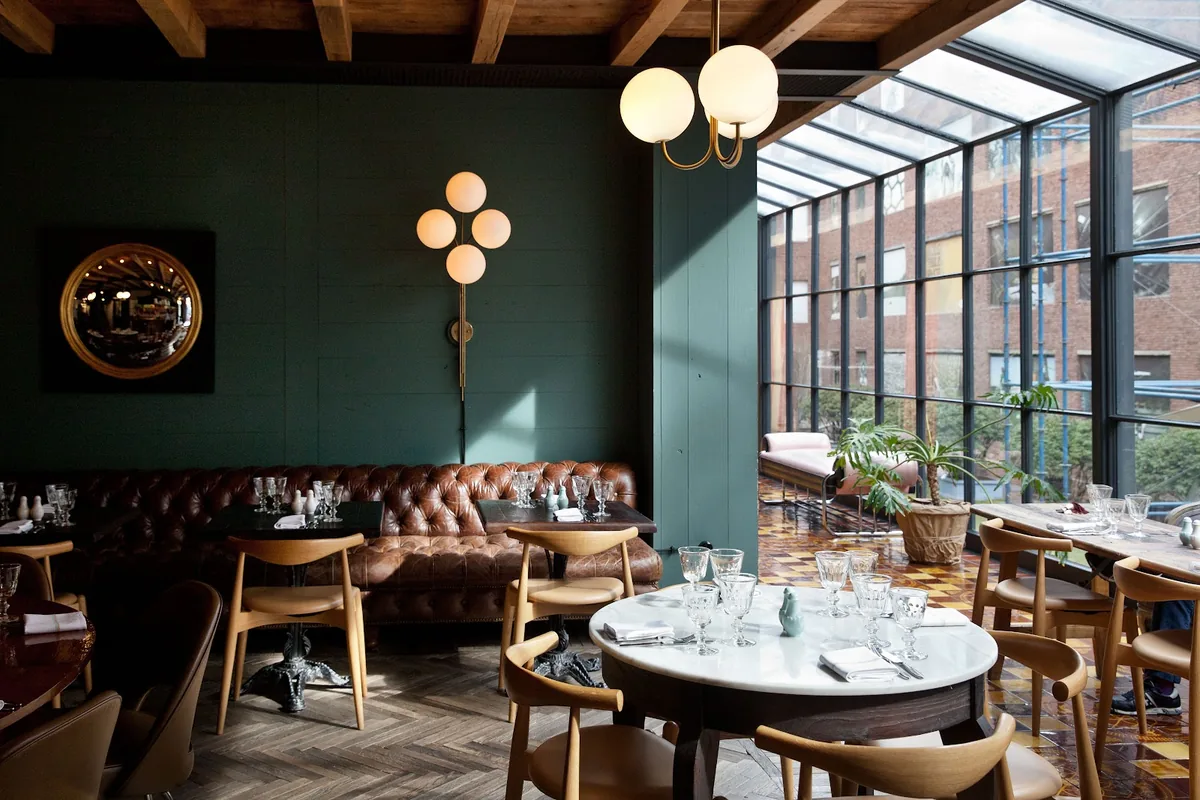 Dining room with a tufted leather banquette and a glass-walled conservatory looking out on red brick at Rooms Hotel Tbilisi