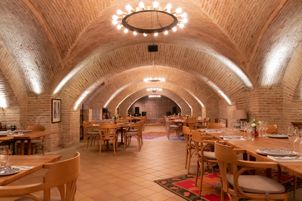 Brick-vaulted dining room with set wooden tables at the Royal Cellar restaurant, Chateau Mukhrani