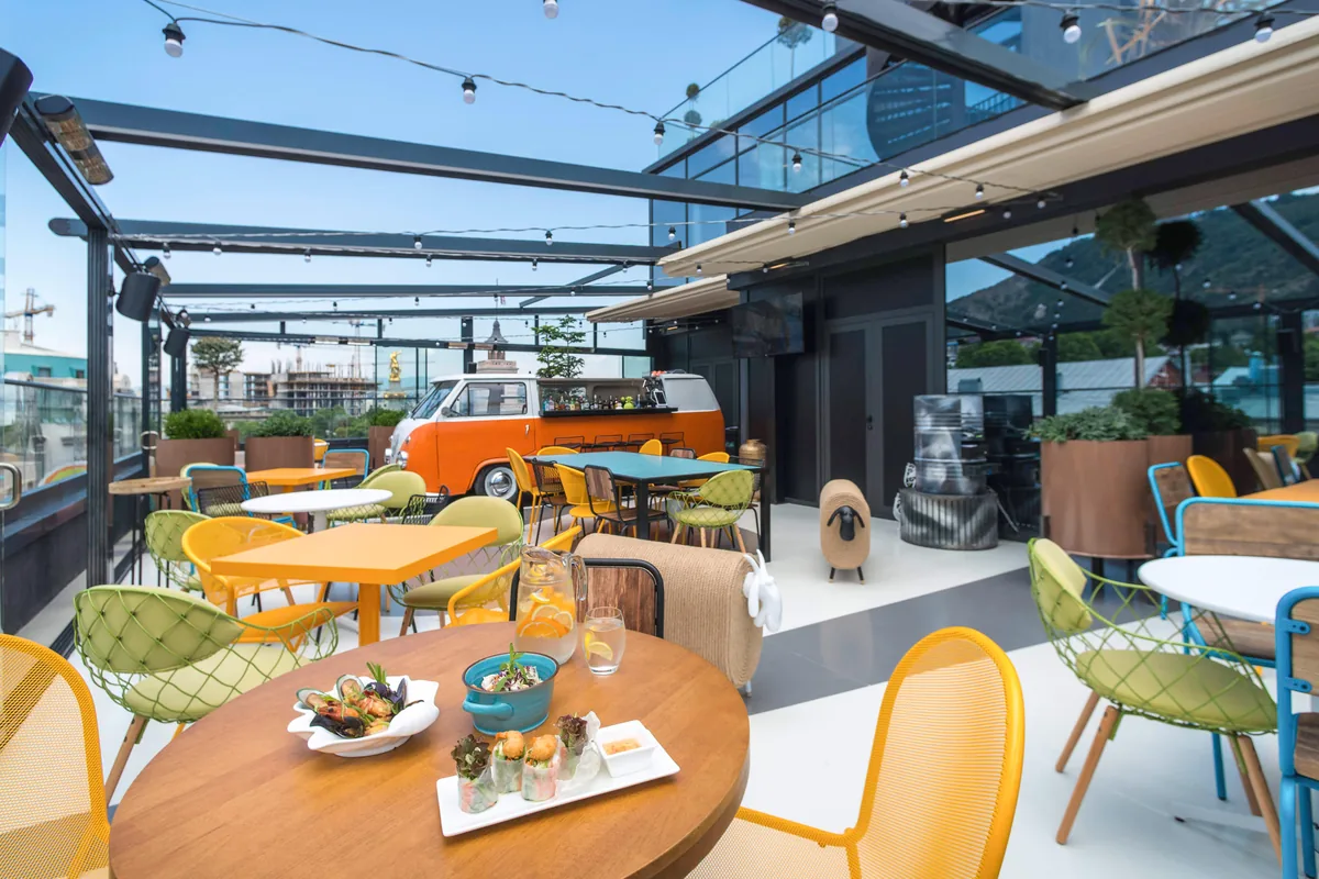 Rooftop terrace with colorful chairs and an orange van bar at Rum Roof Kitchen Bar