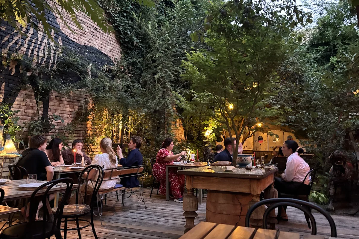 Candlelit garden tables under the trees and the black lion mural in the courtyard at Shavi Lomi