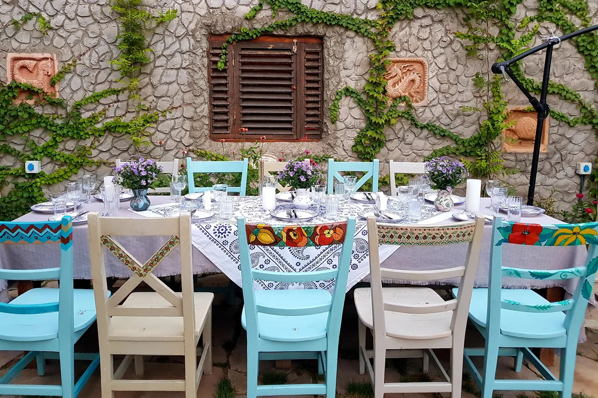 Outdoor table set with painted wooden chairs and stone wall backdrop at Sheen Aura