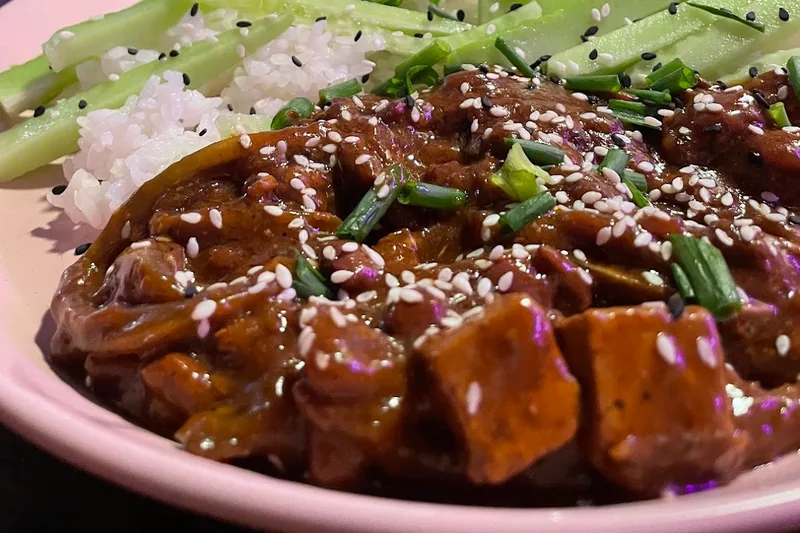 Glazed tofu with cucumber over rice on a pink plate at Shpana