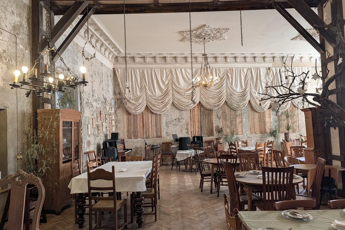The dining room at Sisters in Kutaisi, with peeling plaster walls, wooden beams, a molded ceiling and draped curtains