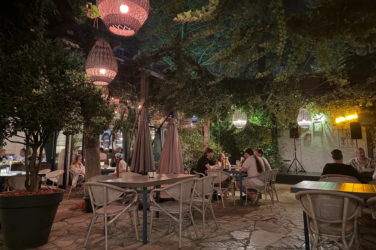 Leafy courtyard terrace with wicker pendant lamps and dining tables at Sormoni