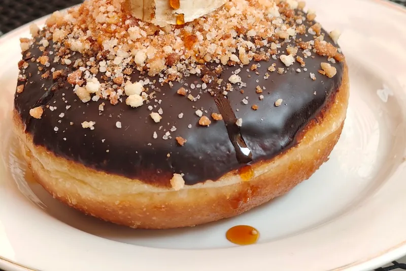 Chocolate glazed doughnut topped with crumbled nuts at Stricha
