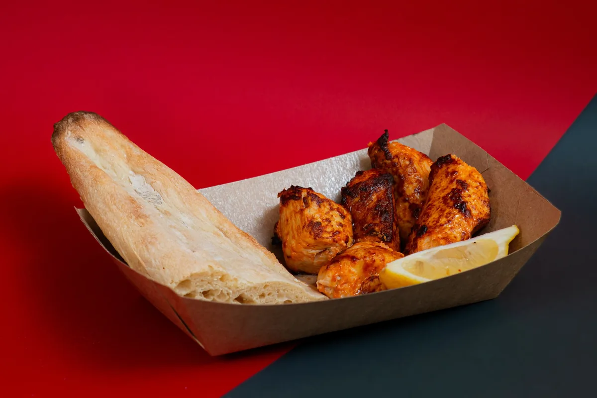 Grilled chicken mtsvadi with a wedge of lemon and a piece of shotis puri in a paper tray at Tsetskhli Ainto, Tbilisi