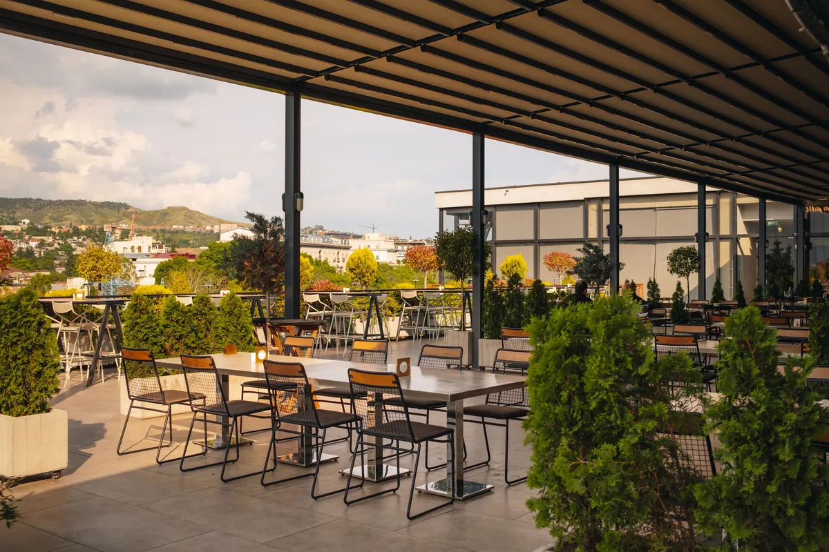 Covered rooftop terrace with outdoor dining tables and city view at Tsiskvili Terrace