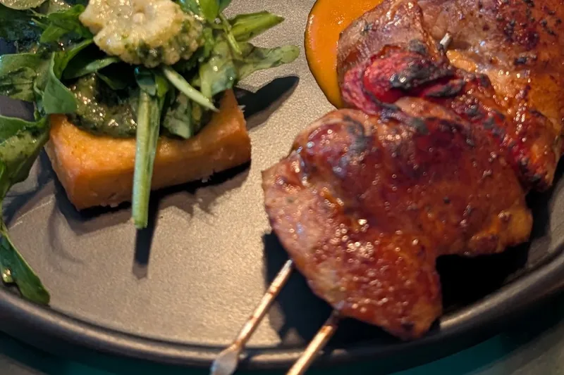 Chicken skewer with tomato tartare and herb salad on a black plate at Van Goghi