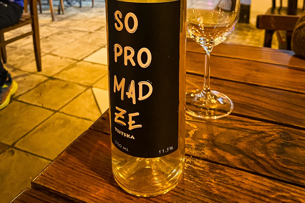 A bottle of Sopromadze Tsitska white wine and an empty wine glass on a wooden table at Vino Underground