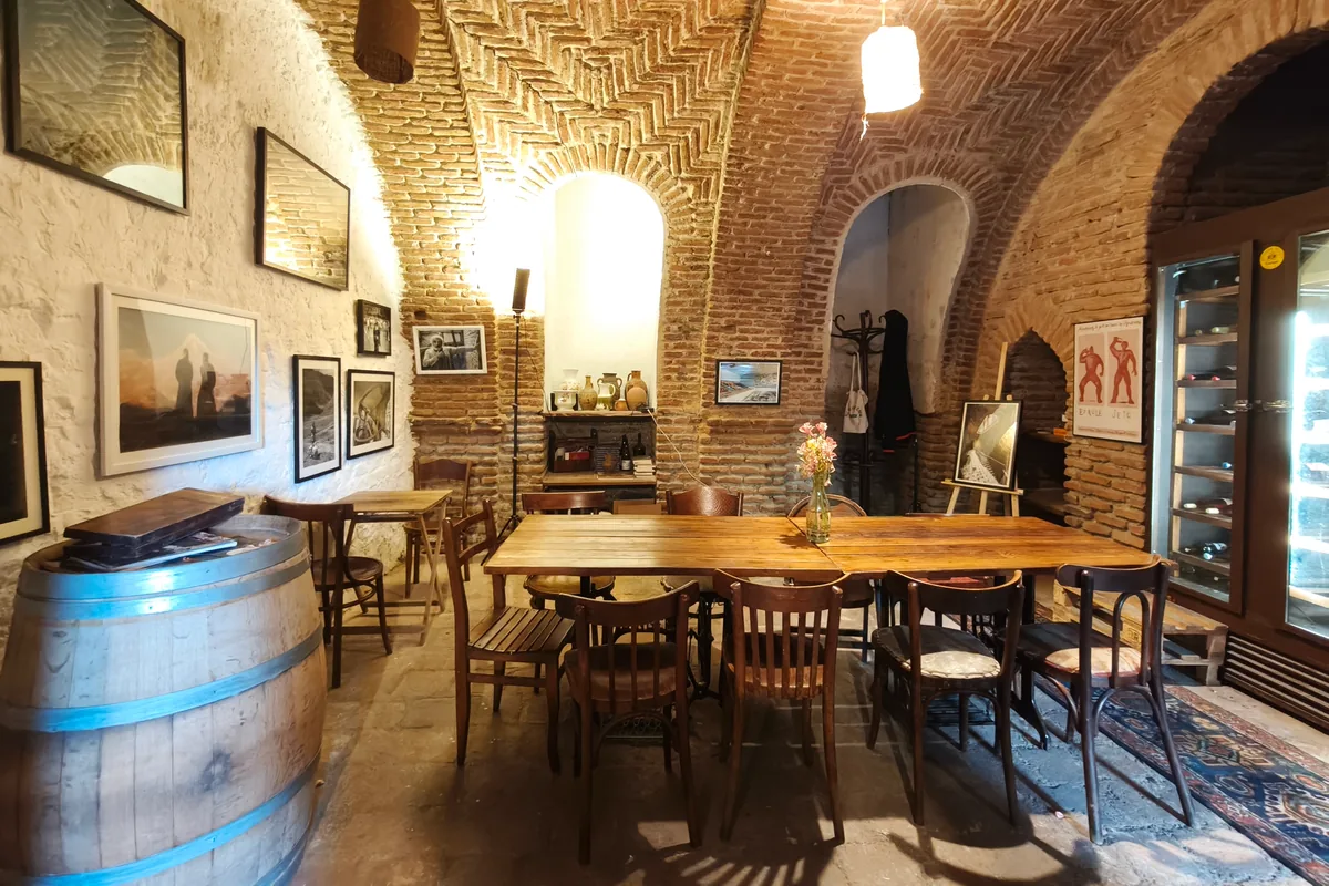 Brick-vaulted cellar room with wooden tables and a wine barrel at Vino Underground