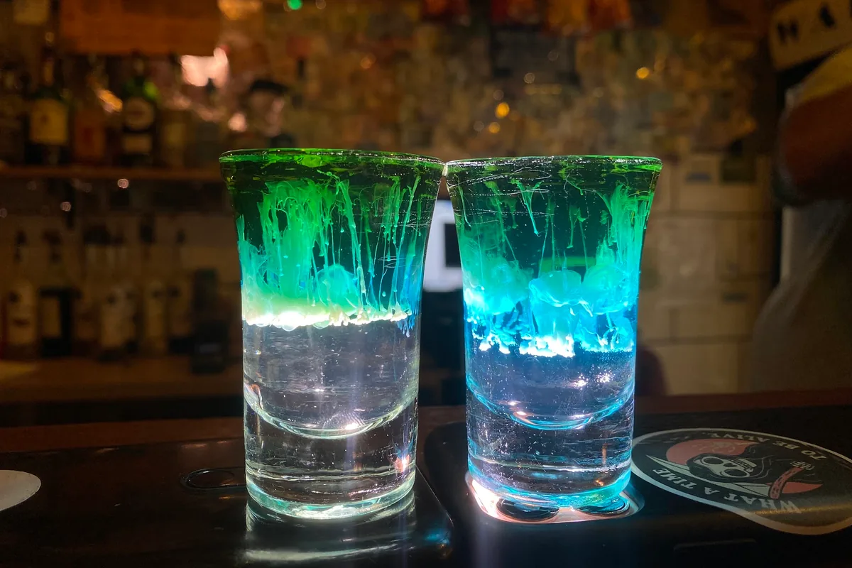 Two layered shot cocktails illuminated by phone screens at Warszawa