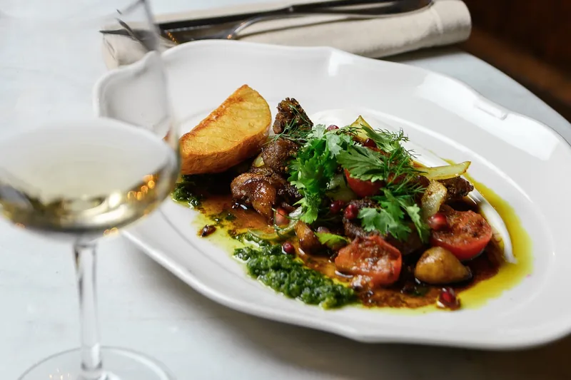 Roasted meat and vegetables on a white platter with a glass of white wine at Weller