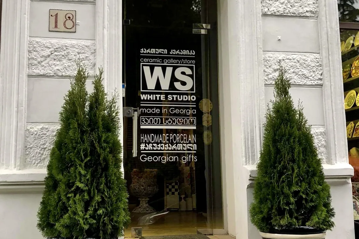 White stucco entrance at number 18 with a glass door lettered for the ceramics store and two cypresses in chevron planters at White Studio Home