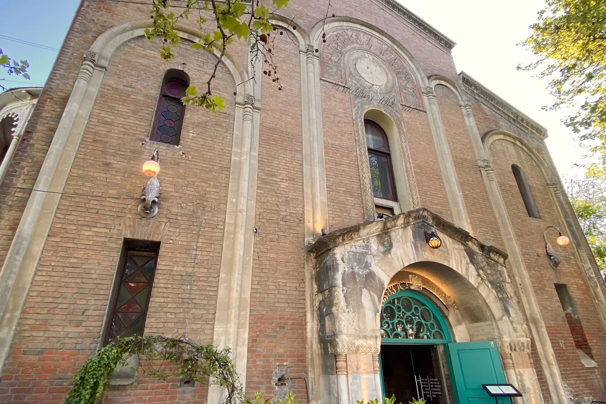 Church-like brick facade with arched windows and a teal arched doorway at Wine Factory N1