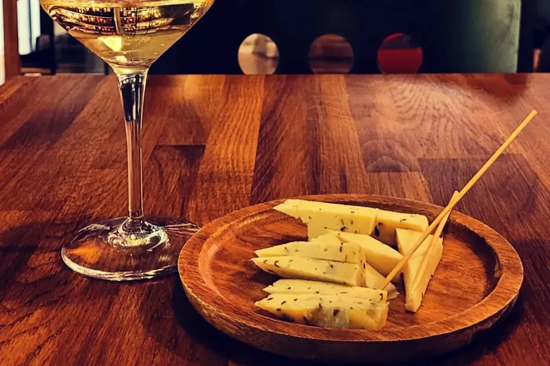 A glass of white wine beside a small wooden plate of sliced herb cheese at Wine Point