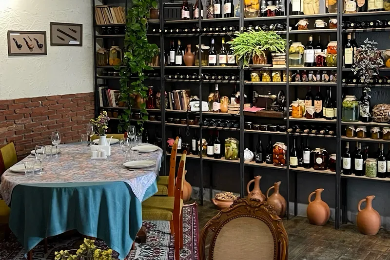 Dining room at Wine Point with a set table and shelves of wine bottles, preserves and clay jugs