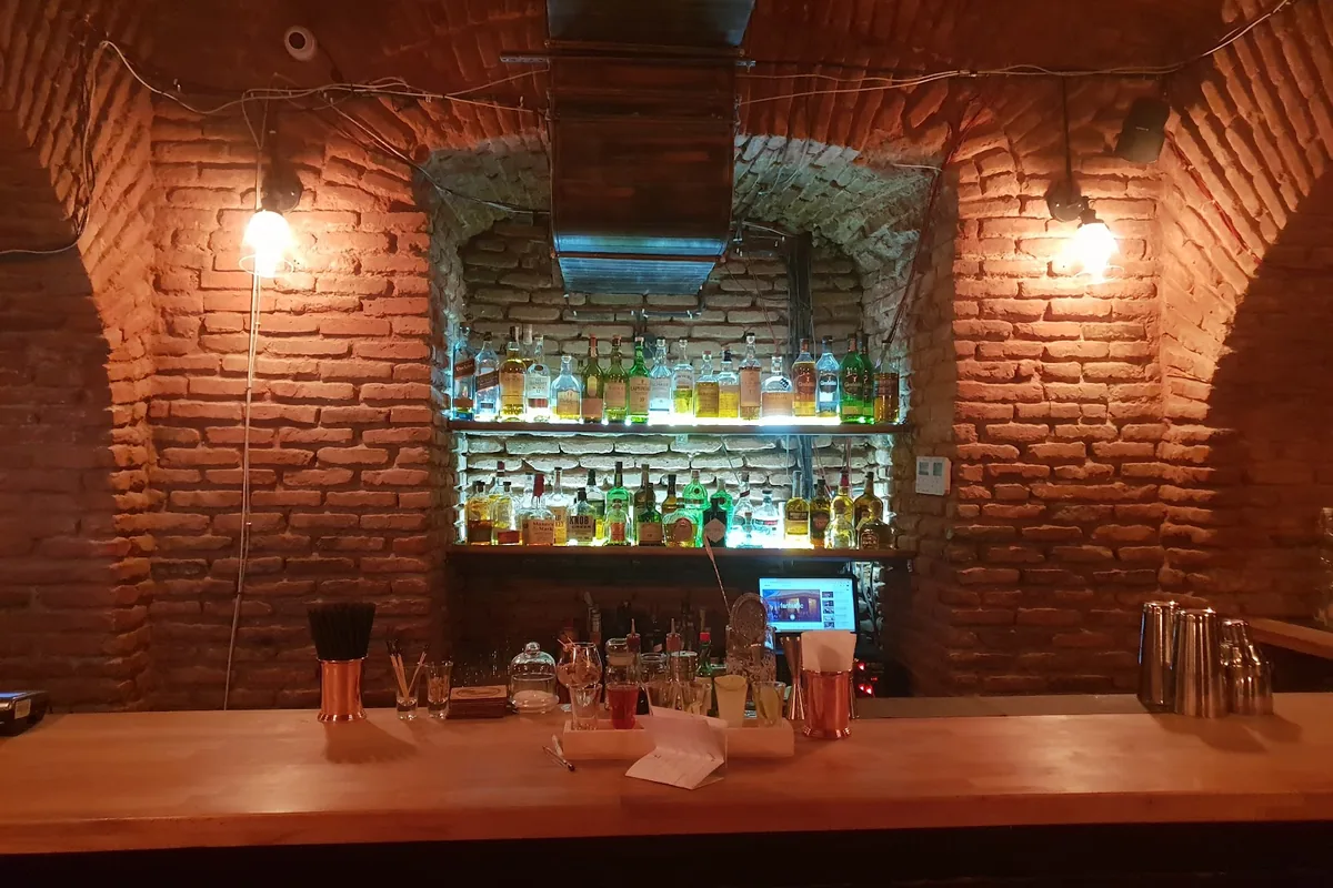 Brick-vaulted cellar bar with a lit back shelf of bottles at Woland's Speakeasy in Sololaki