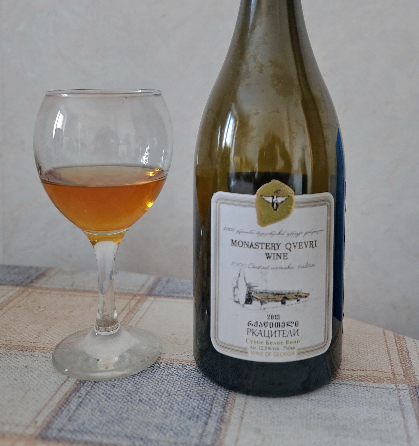 A glass of amber Rkatsiteli wine next to a bottle of Monastery Qvevri Wine labelled dry white