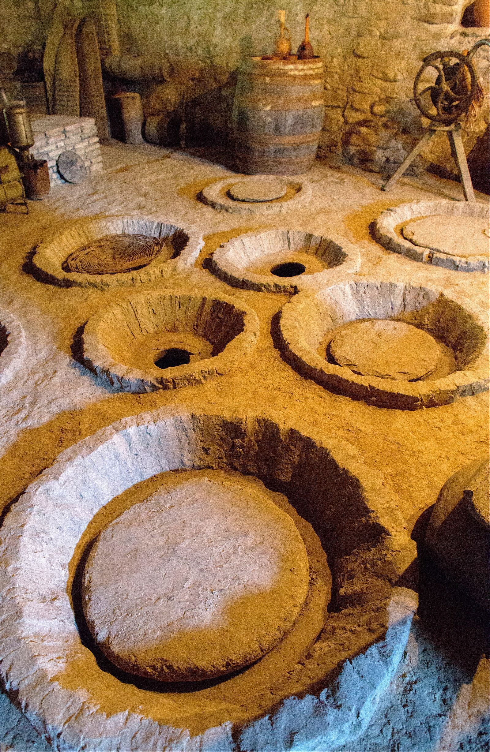 Rows of qvevri, clay wine jars, buried to their rims in a cellar floor in Velistsikhe, Kakheti, some open and some closed with round lids