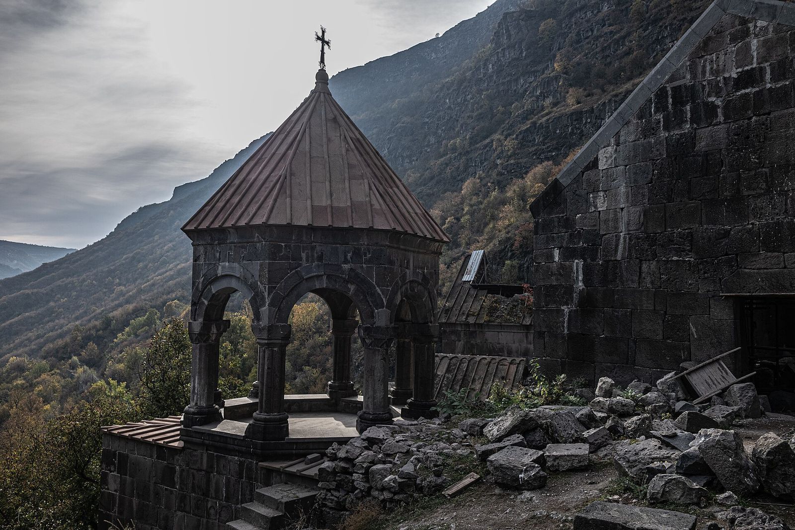 The arched stone bell tower of Kobayr Monastery on a ledge above the wooded Debed canyon in autumn