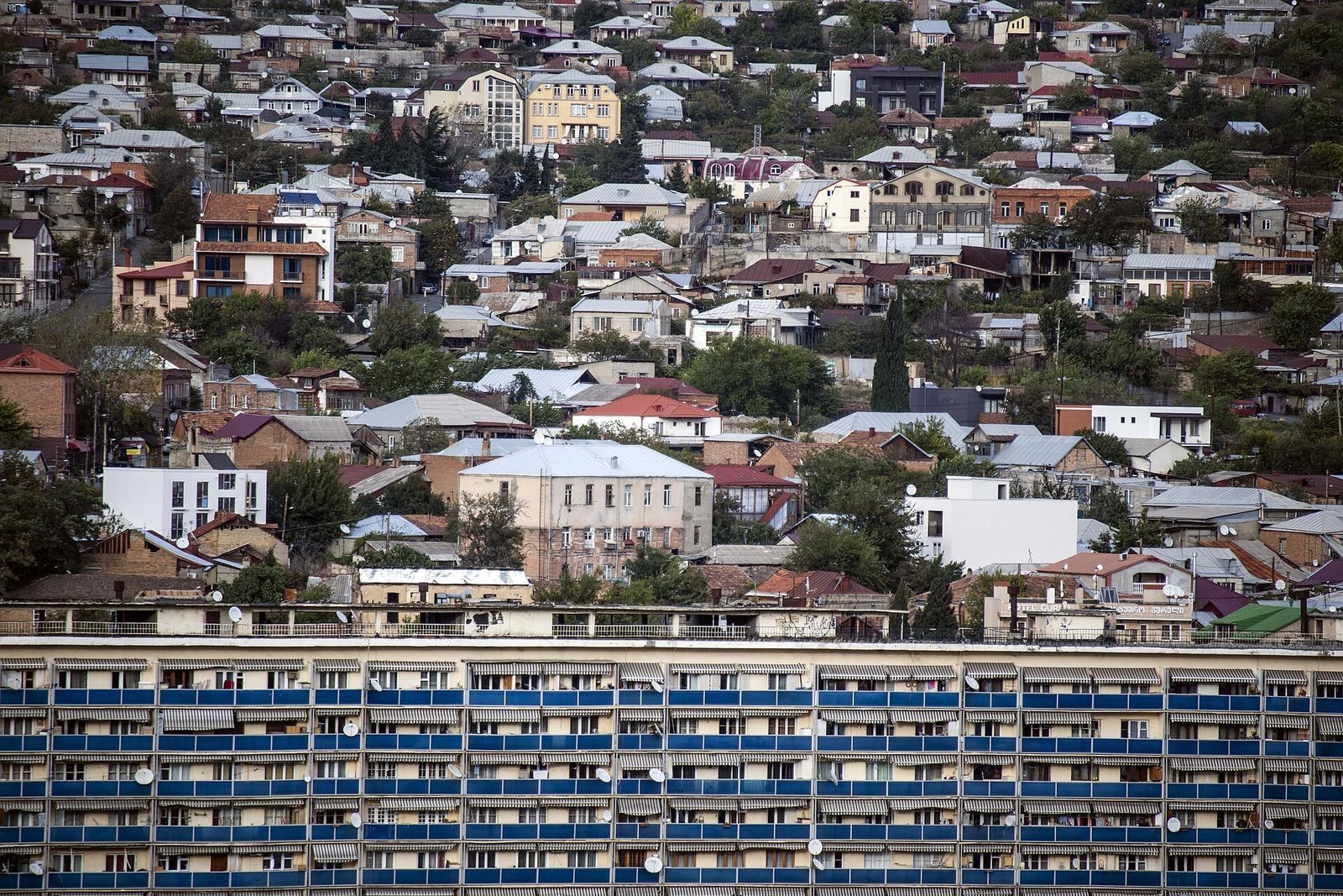Houses with tin roofs climbing the Avlabari hillside above a long Soviet apartment block with blue balconies