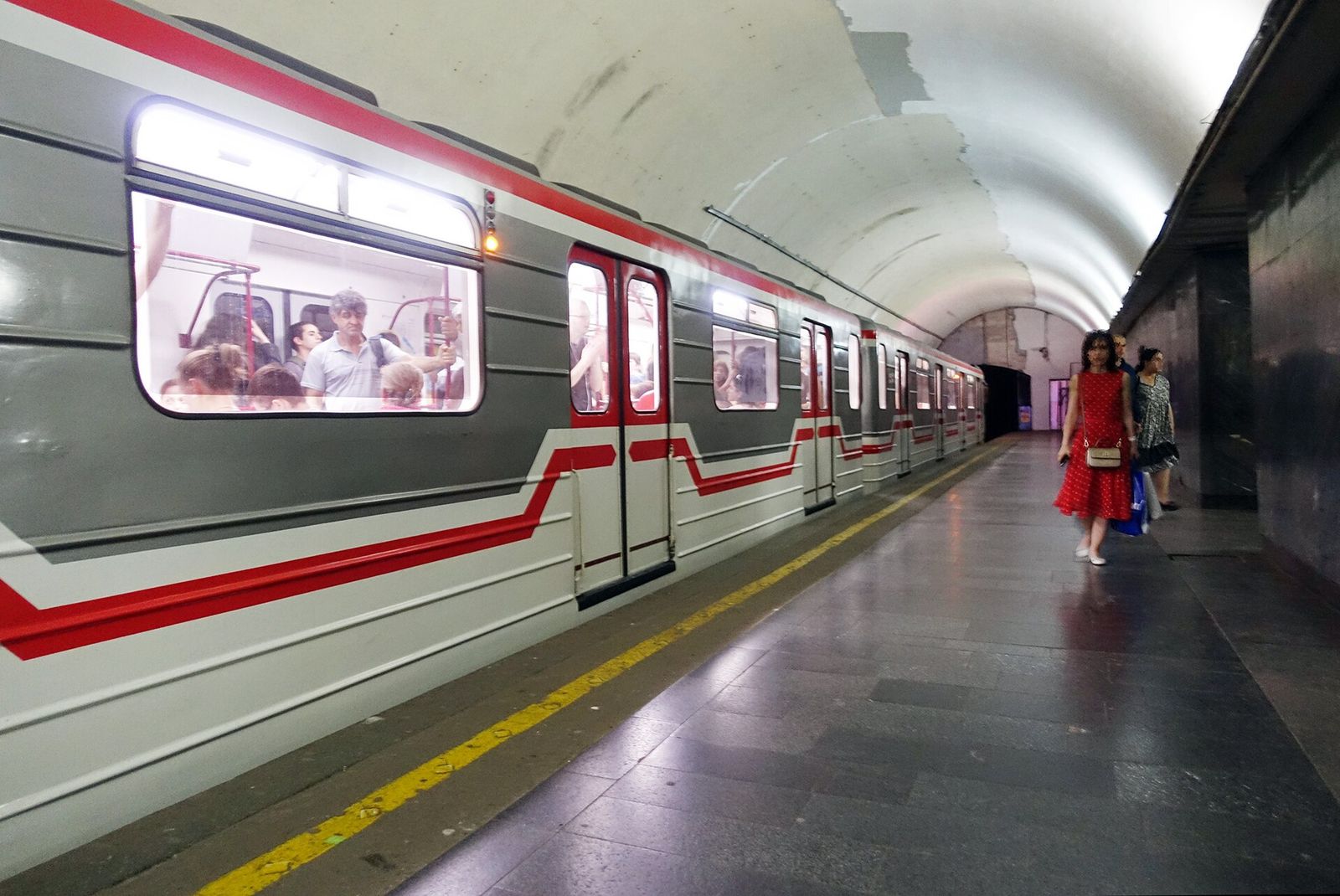 A red and white Tbilisi metro train at the platform of Avlabari station under a white vaulted ceiling