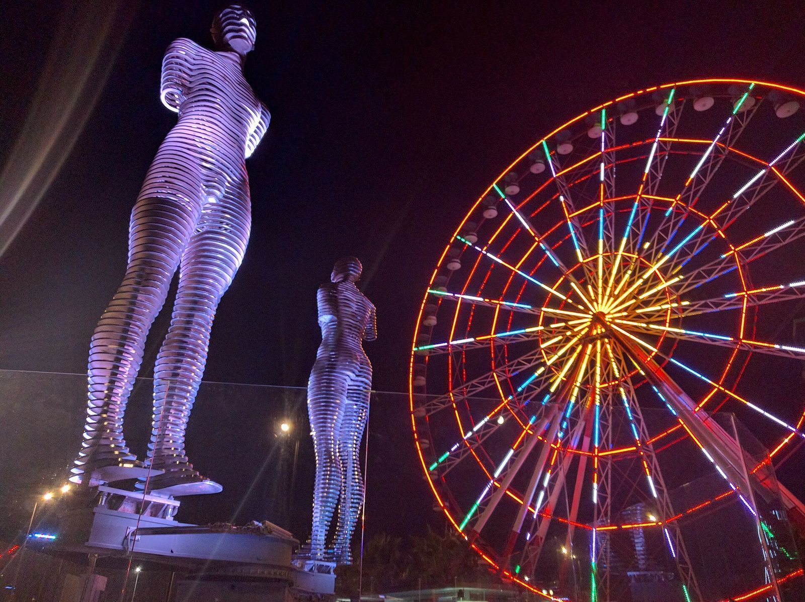 The lit steel statues of Ali and Nino beside the Ferris wheel on Batumi's seafront at night