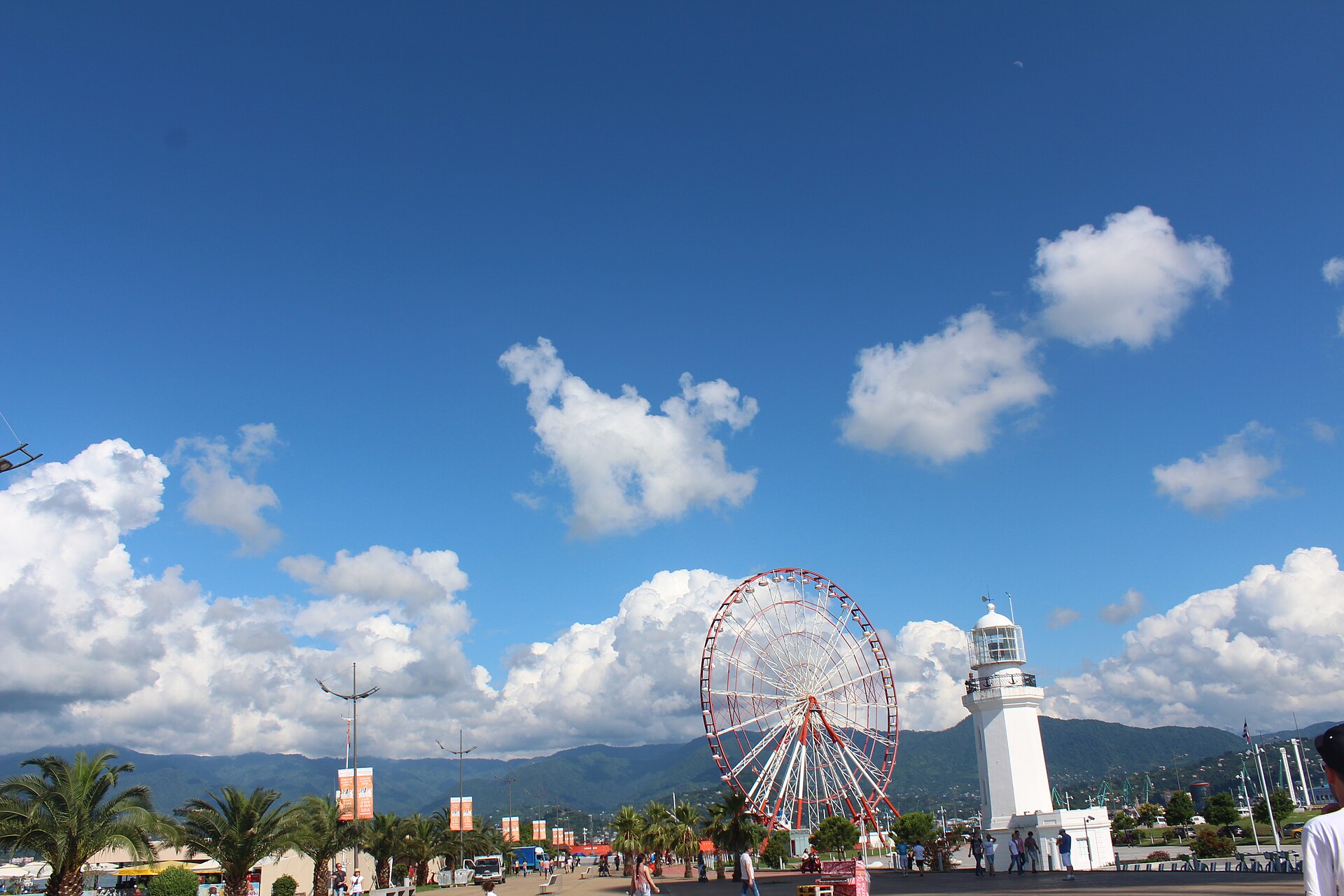 The Ferris wheel and the white 19th century lighthouse in Batumi's Miracle Park under a blue sky