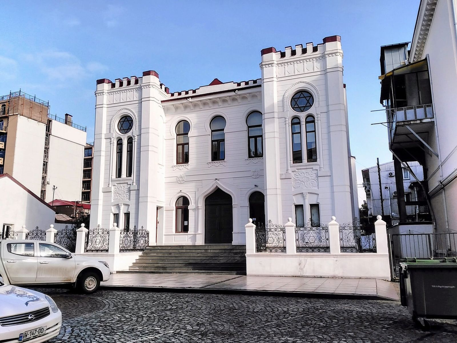 The white facade of Batumi Synagogue with its two crenellated towers and Star of David windows, behind a wrought iron fence