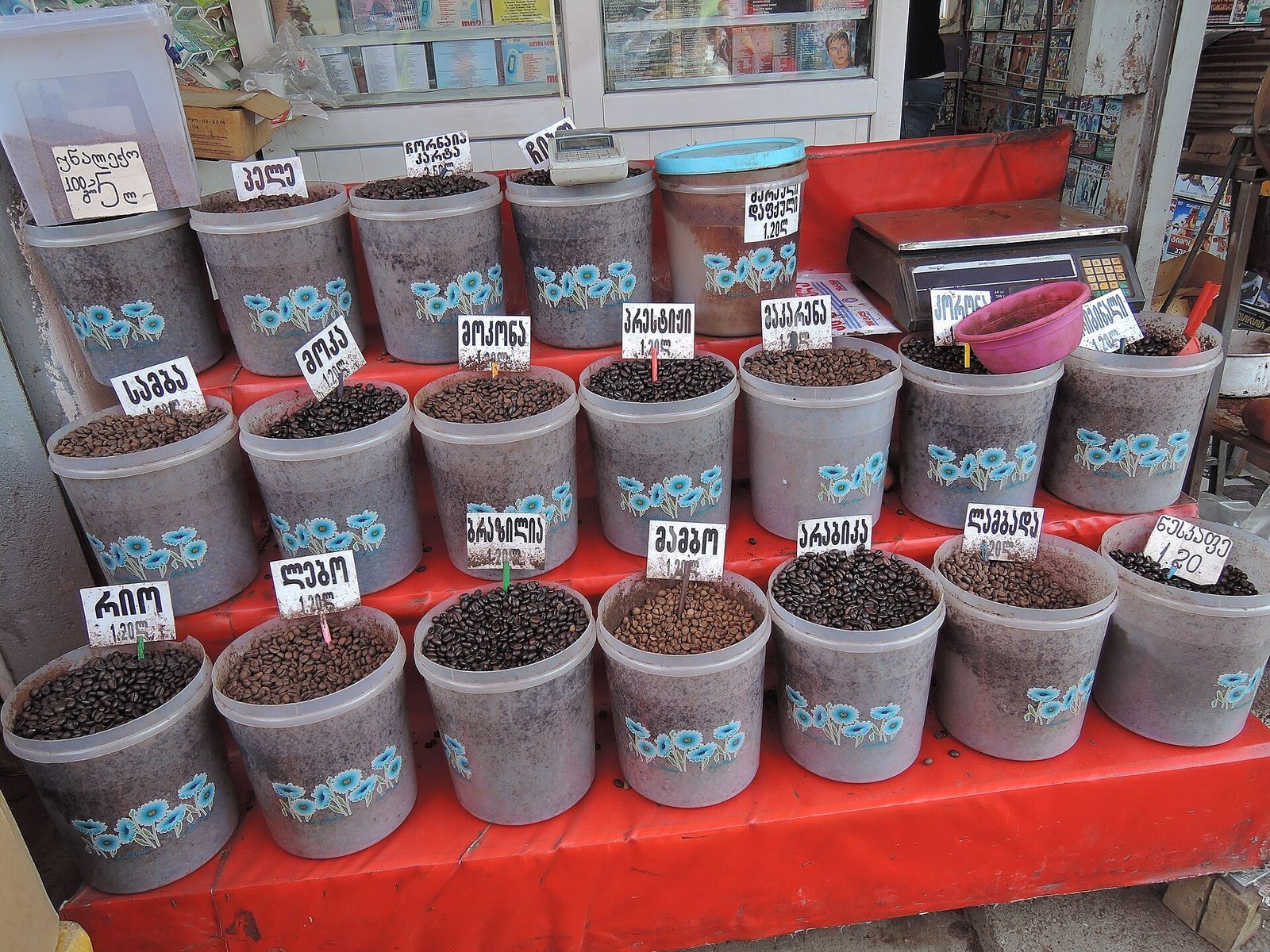 Loose coffee beans sold by weight from labeled tubs at a stall in Tbilisi