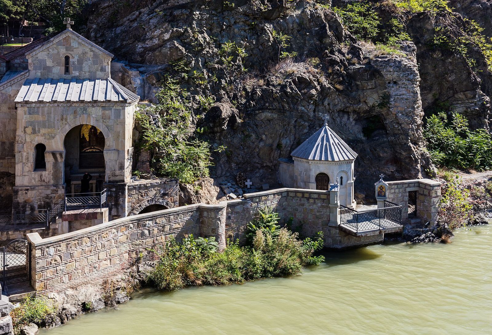 The St Abo Tbileli chapel built into the cliff under Metekhi, with the saint's gold mosaic in its arch and a small terrace over the river