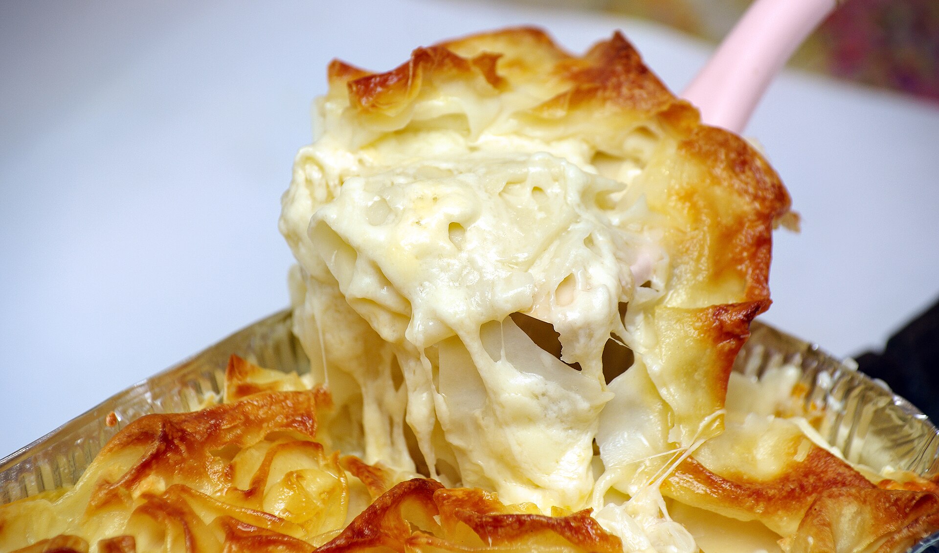 A serving of achma lifted from its tray, thin layers of dough and stretchy melted cheese under a browned top