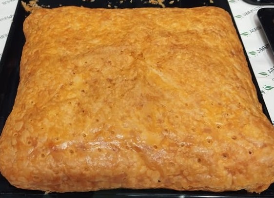 A square penovani khachapuri on a baking tray, the puff pastry baked golden and blistered on top