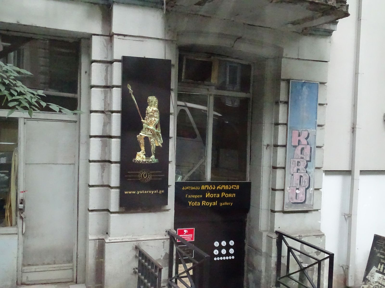 The street entrance of the Yota Royal Gallery on Shalva Dadiani Street, with its signboard and a gold knight figure above the steps down to the basement