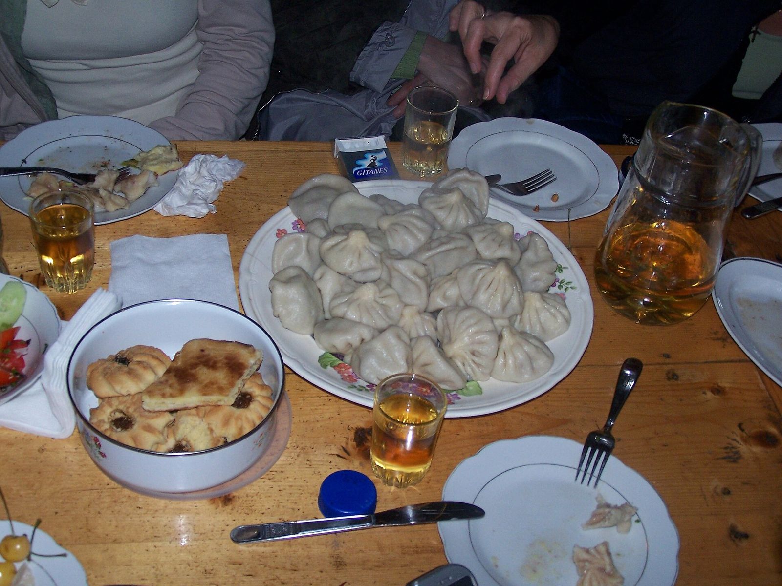 A large plate of khinkali shared on a restaurant table, with bread, glasses and side plates around it