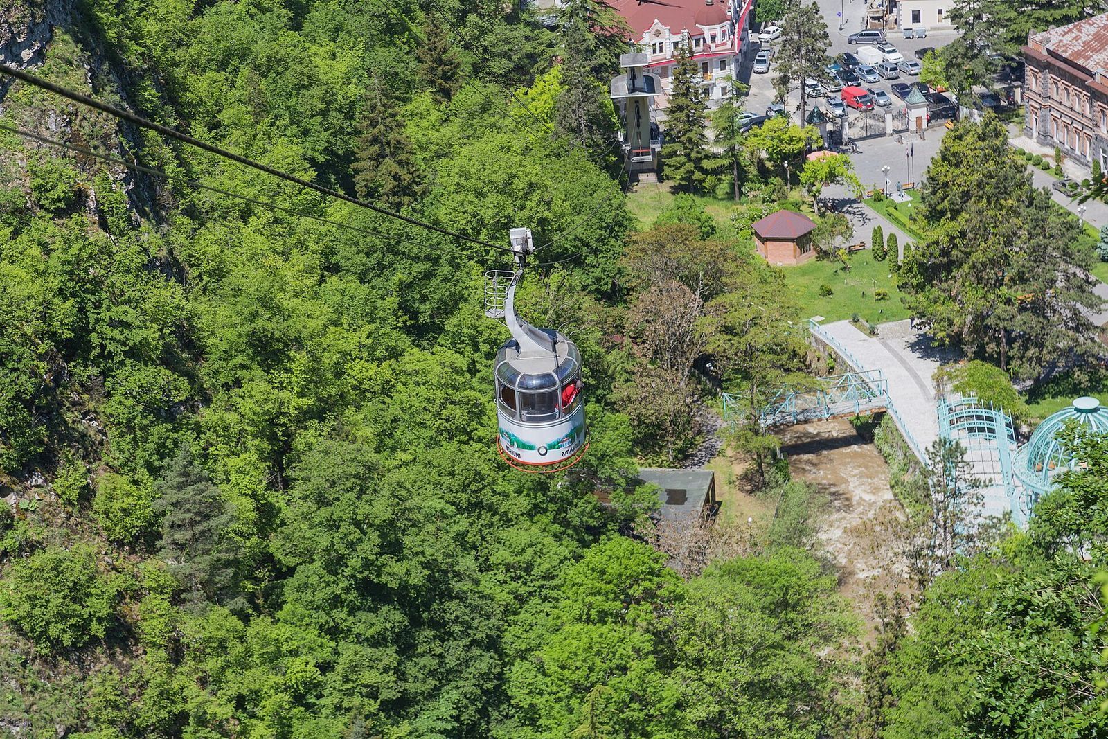 A Borjomi cable car cabin climbing over the treetops above the footbridges and spring pavilion of Central Park