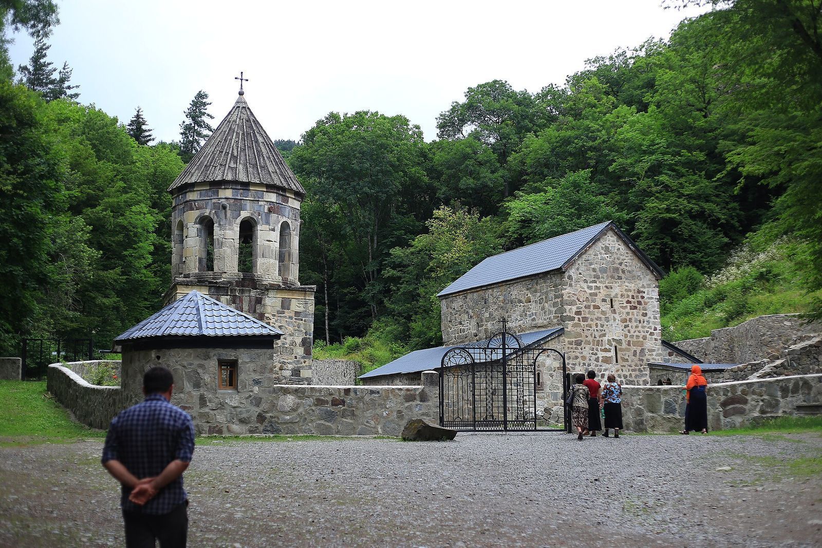The Green Monastery near Borjomi: a stone bell tower and small church with grey roofs in a forest clearing
