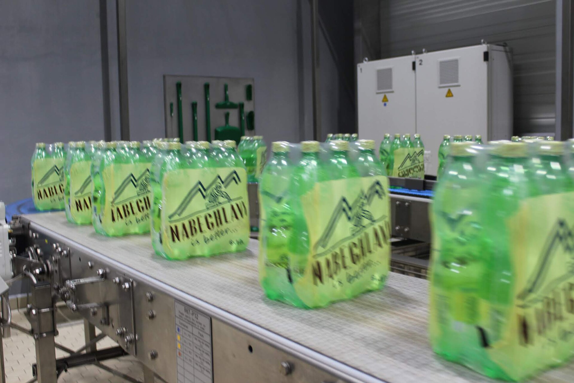 Packs of Nabeghlavi mineral water in green bottles with the mountain logo on the bottling line