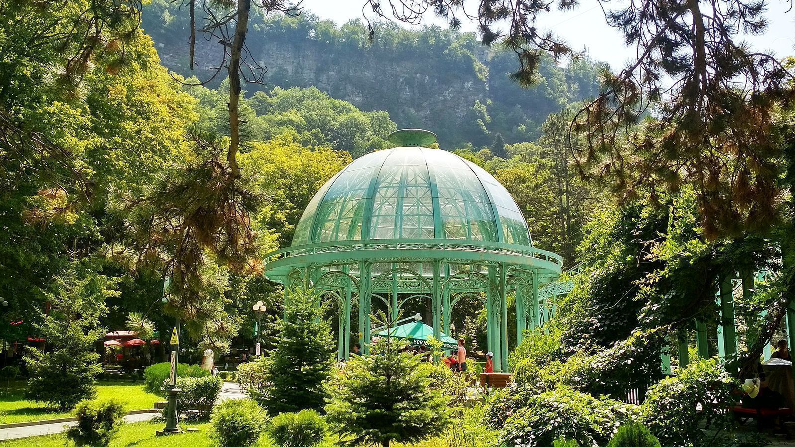 The green glass-domed pavilion over the main mineral spring in Borjomi Central Park, among pines below a wooded cliff