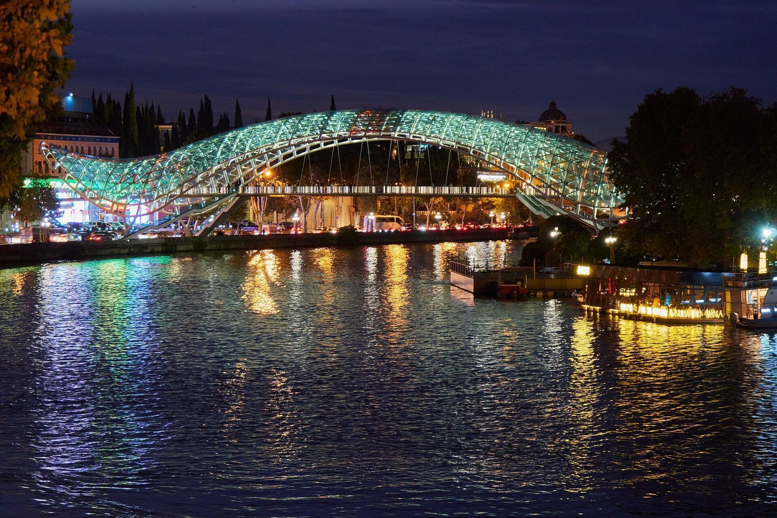 The Bridge of Peace, a pedestrian bridge over the Mtkvari River, illuminated at night.