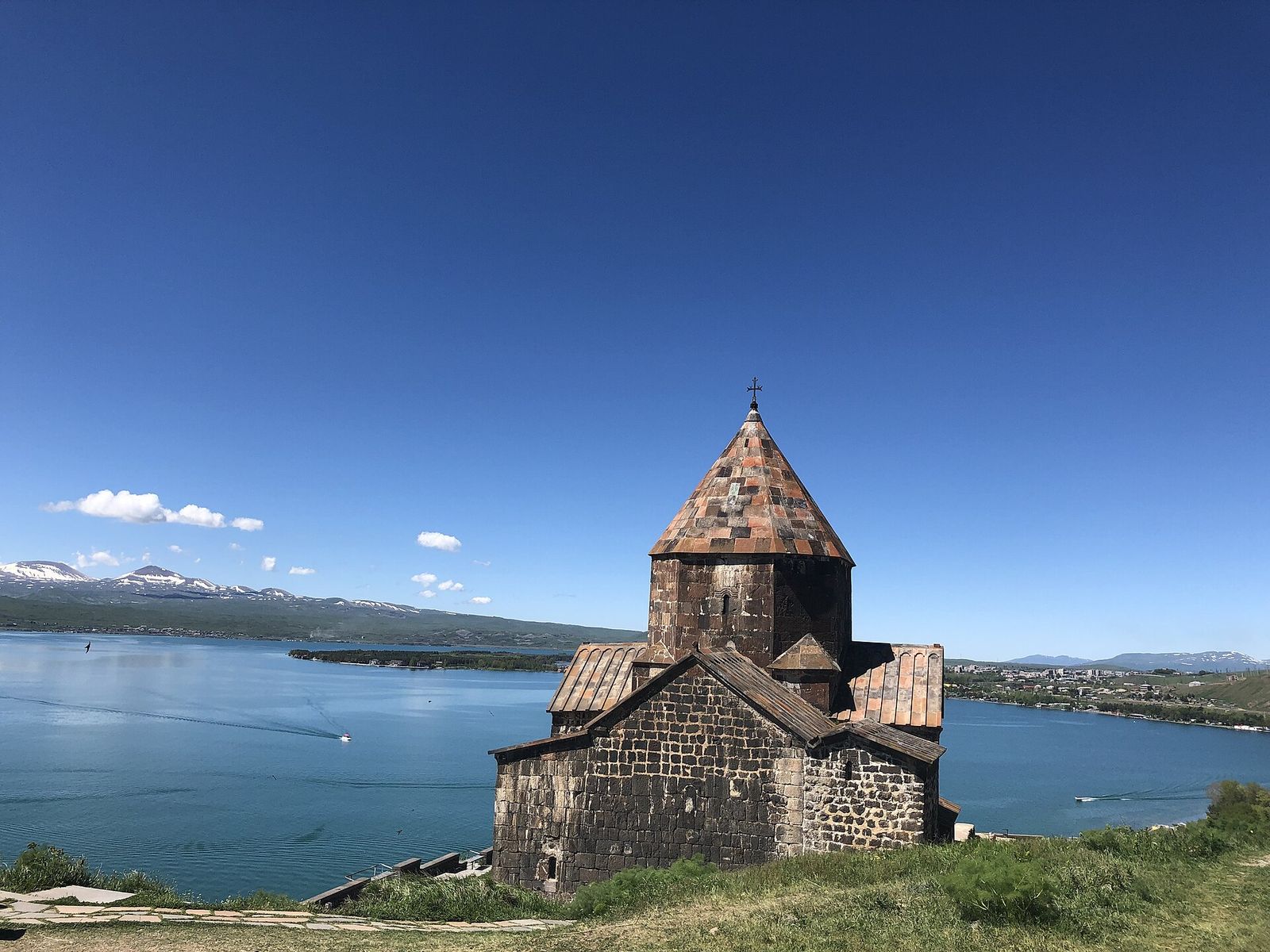 A dark stone church of Sevanavank on its peninsula above the blue water of Lake Sevan, Armenia