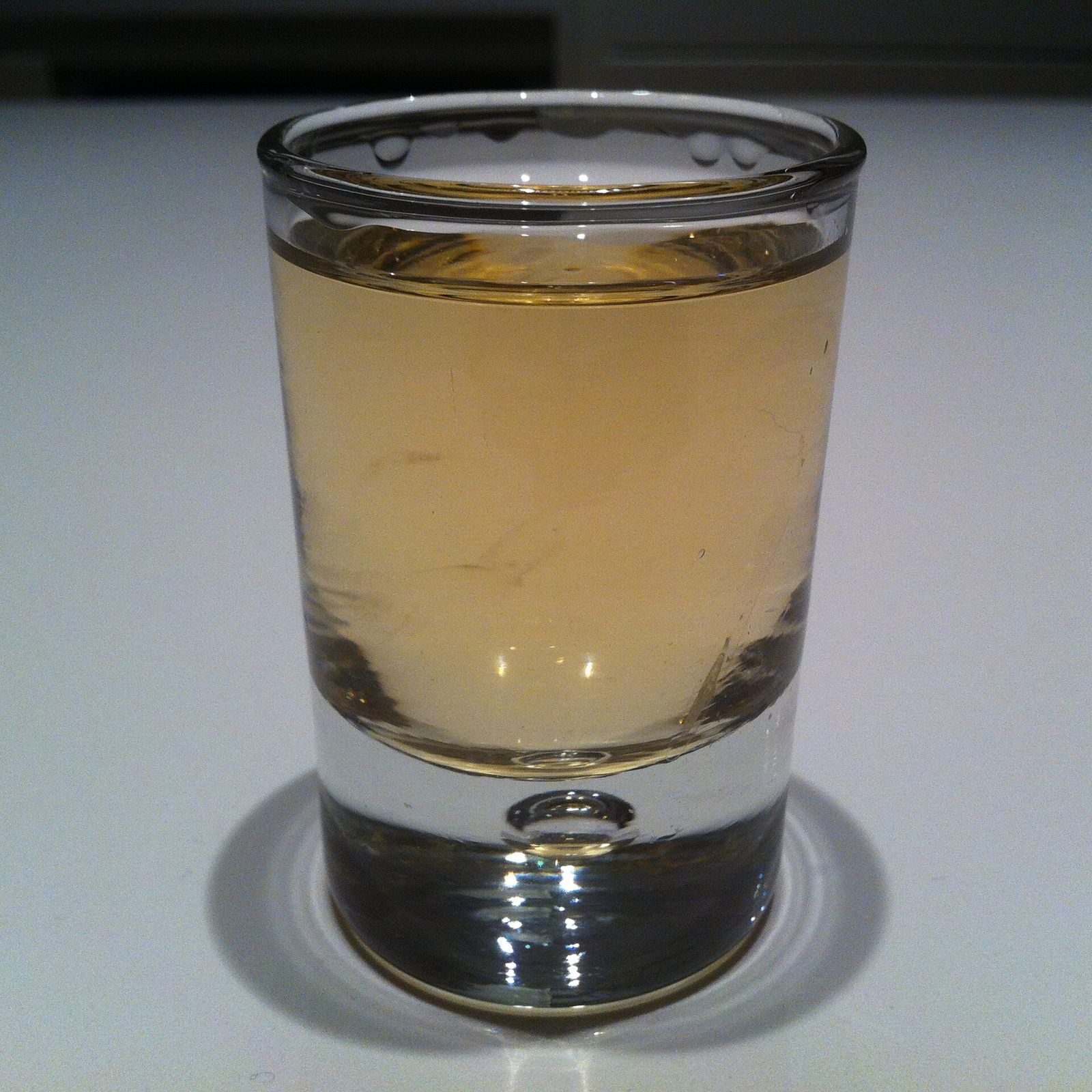 A small shot glass filled with pale golden chacha on a white table