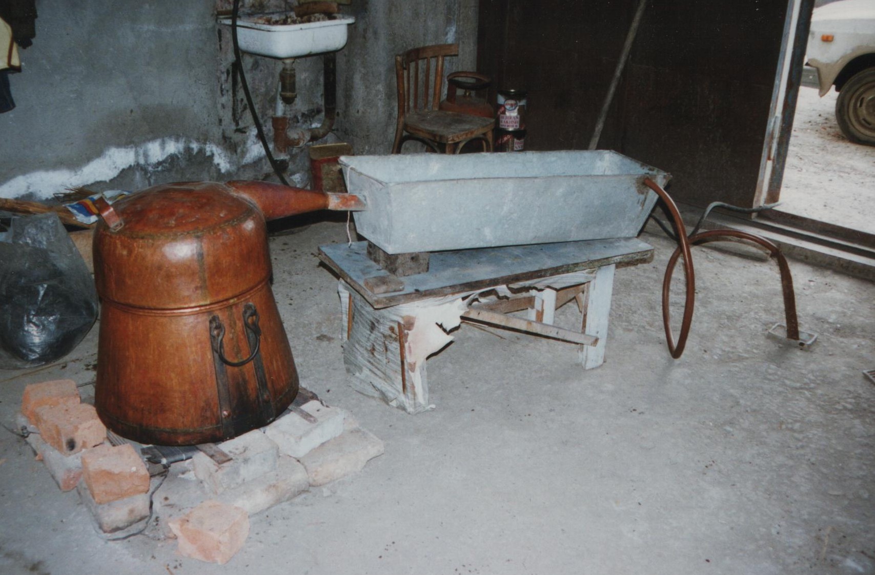 A copper pot still and a metal cooling trough set up for distilling chacha at home in Georgia